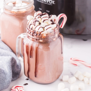 Slow cooker hot chocolate in a glass mug with marshmallows, a candy cane, and chocolate syrup