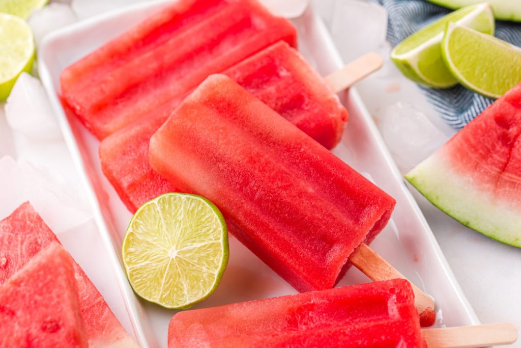 red popsicles sitting in a tray with a lime and watermelon slices in the background