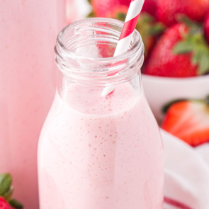pink strawberry milk in a glass milk bottle with a red and white straw
