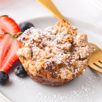 French toast muffin topped with powdered sugar on a plate with strawberries, blueberries and a copper fork